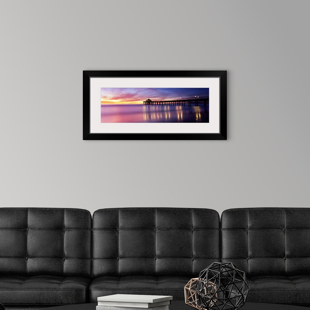 A modern room featuring Panoramic photograph of pier extending into ocean at sunset. The lights on the pier are reflected...