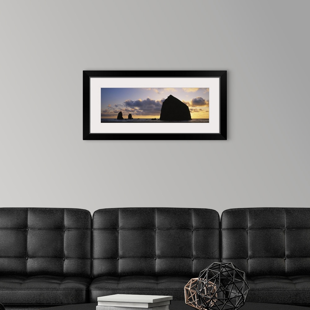 A modern room featuring Large panoramic piece of the sunset that silhouettes rock formations in the ocean.