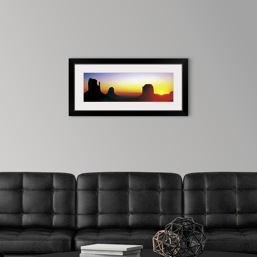 A modern room featuring The sun begins to rise and silhouette Monument Valley in a wide angle view.