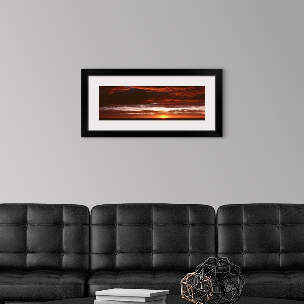 A modern room featuring Panoramic photograph of a sunset just hitting the horizon and lighting up a cloud filled sky with...