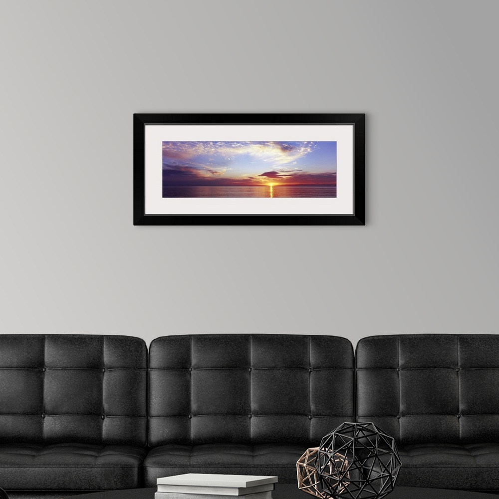 A modern room featuring Large panoramic photograph of a sunset over the ocean with a cloud filled sky.