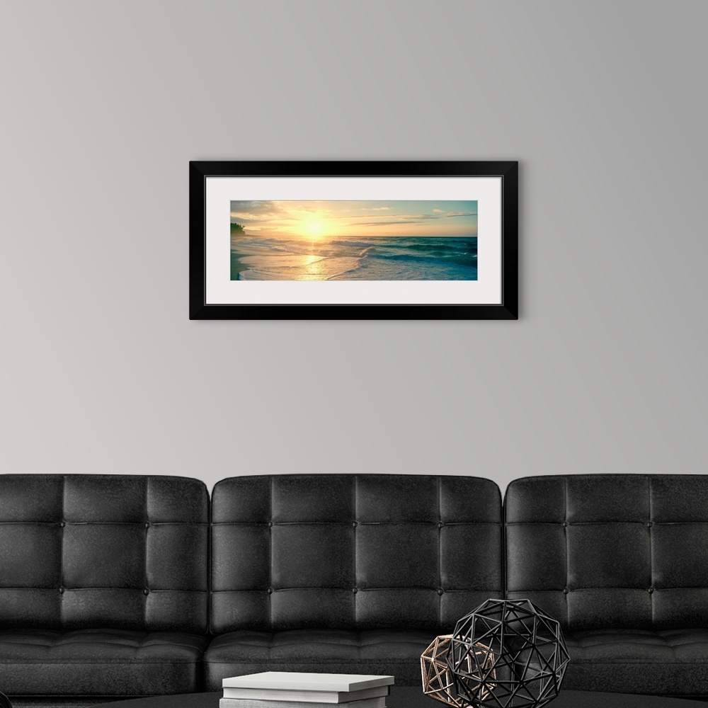 A modern room featuring Long panoramic print of an intense setting sun going down over the ocean with waves washing ashor...