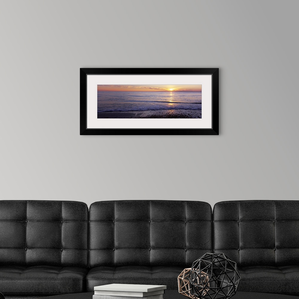 A modern room featuring This is a panoramic landscape photograph of waves softly washing up on the shore of a sandy beach.
