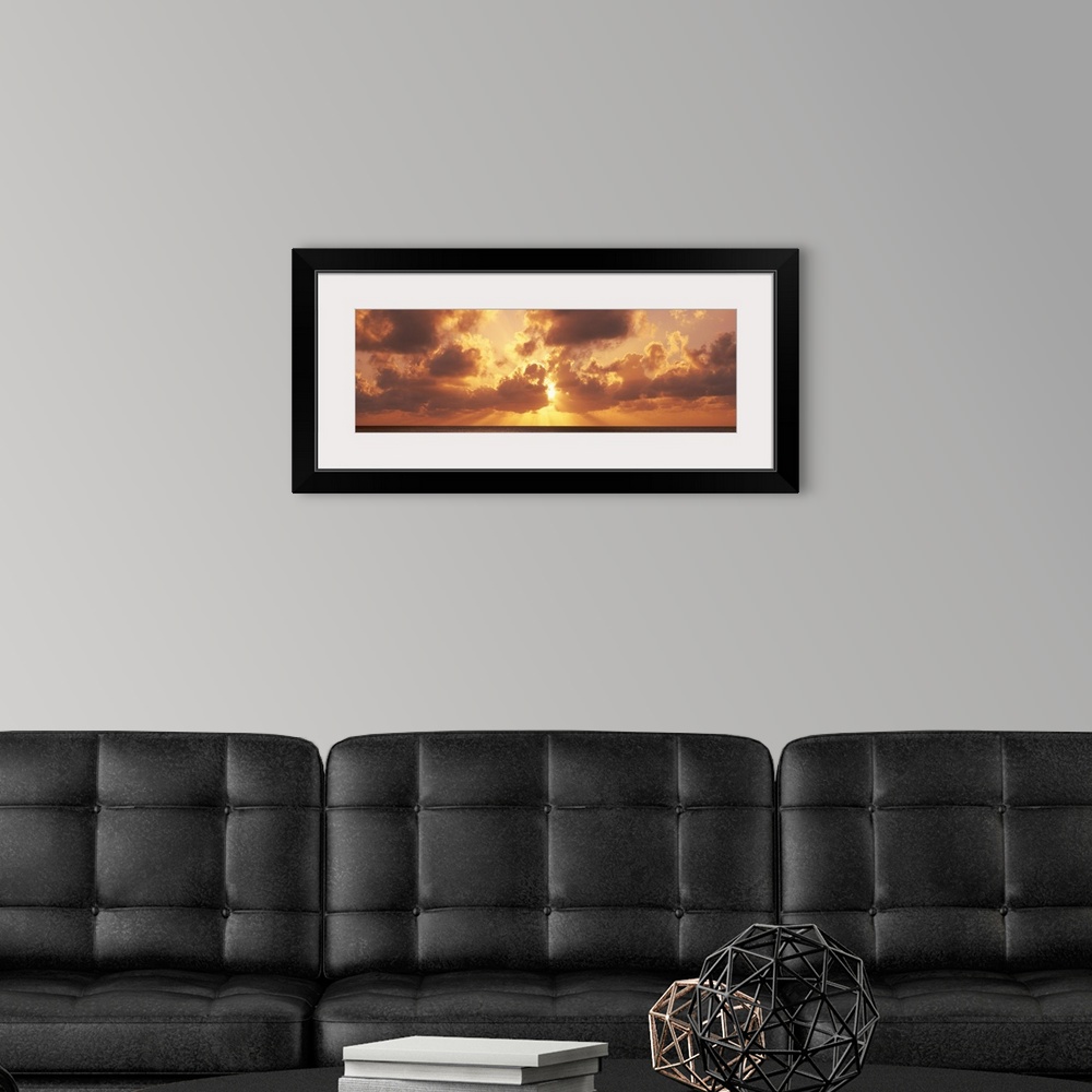 A modern room featuring Large panoramic photograph taken of a sunset behind the clouds with its rays bursting through and...