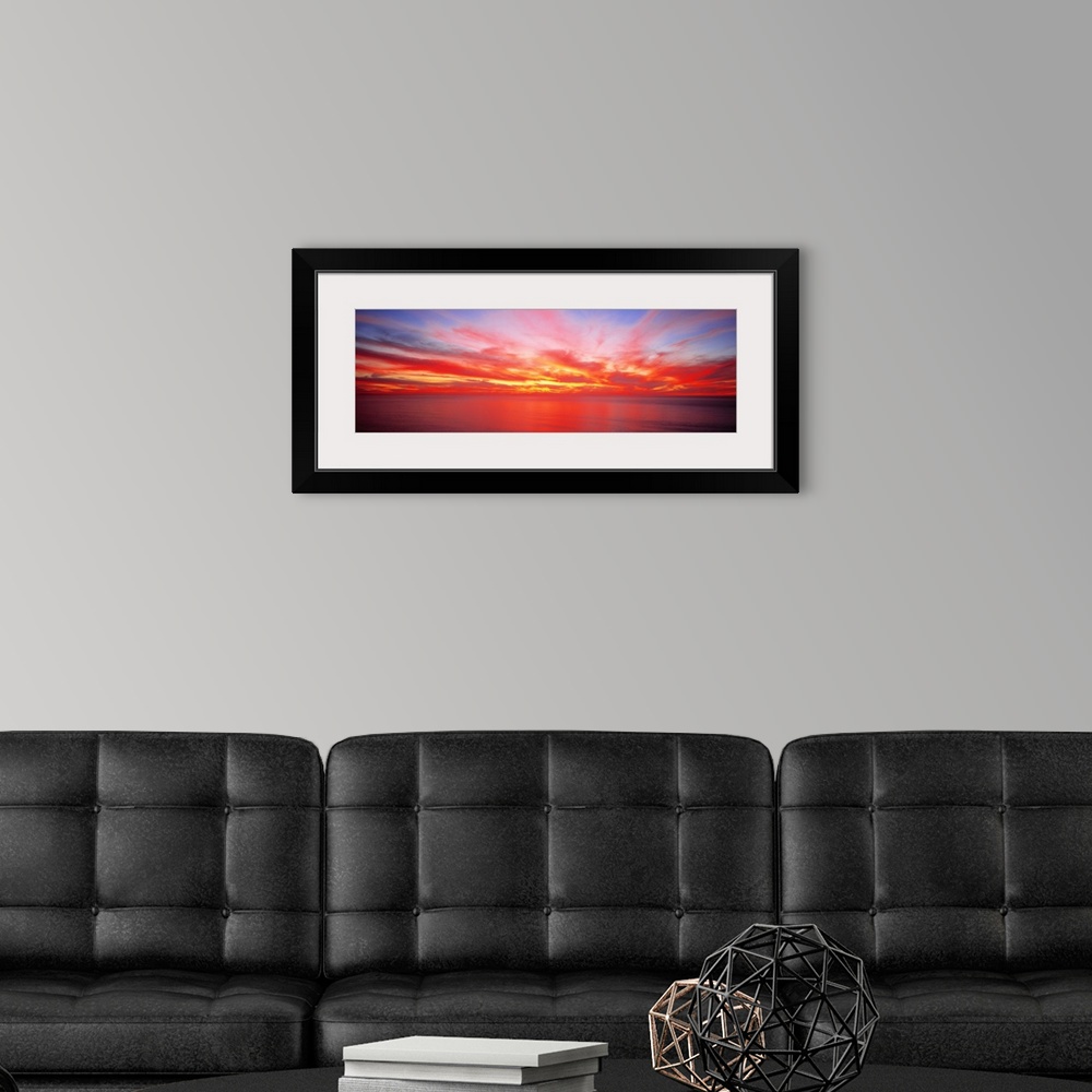 A modern room featuring Wide angle photograph on a giant wall hanging of the sky full of streaking clouds during a vibran...