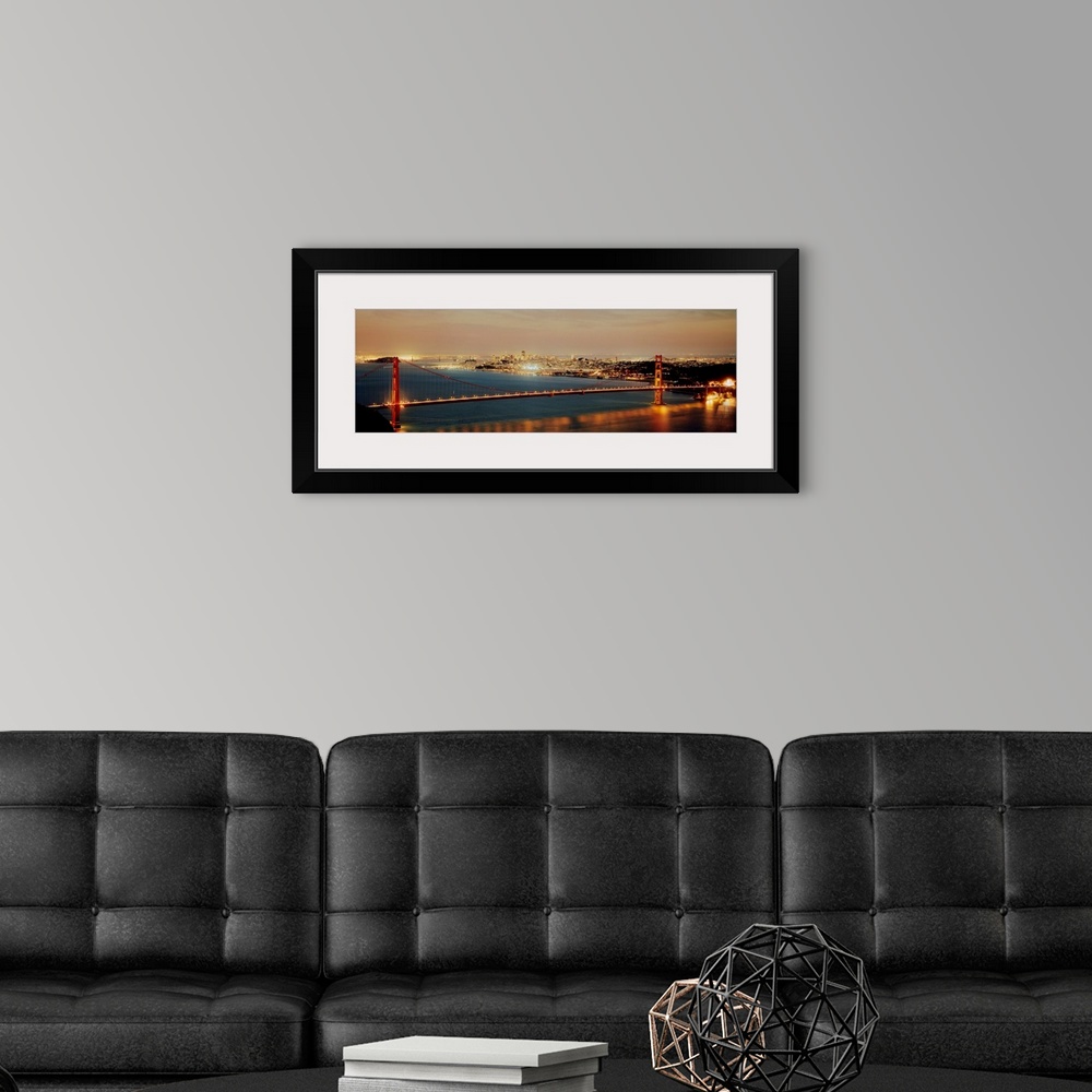 A modern room featuring Panoramic photograph shows the bright lights of the Golden Gate bridge as they reflect onto the w...