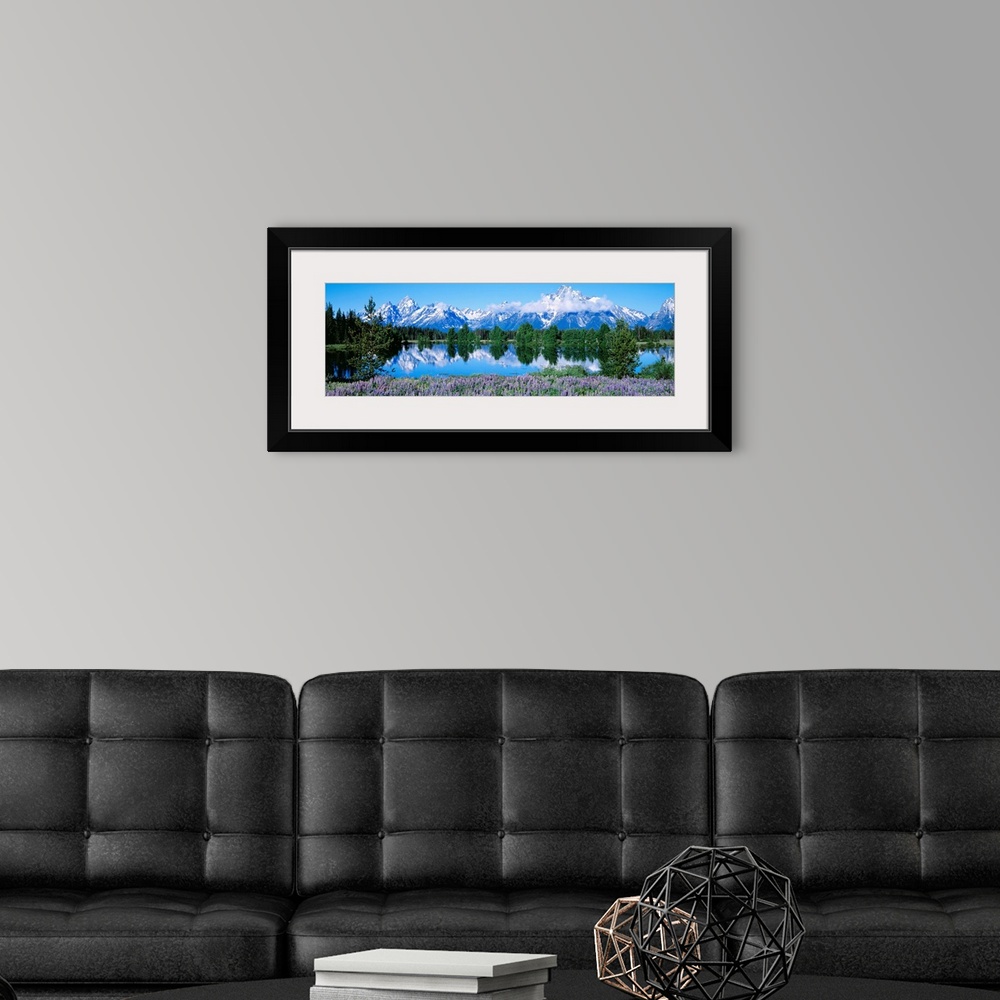 A modern room featuring This panoramic landscape photograph shows wildflowers growing around a lake that reflects the tre...