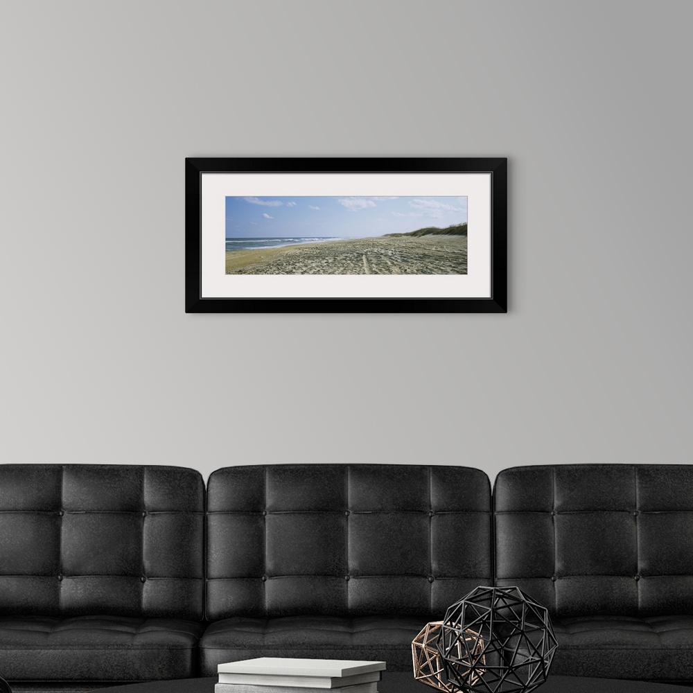 A modern room featuring A panoramic photograph of a sandy beach indented with footsteps and tracks down to the ocean water.