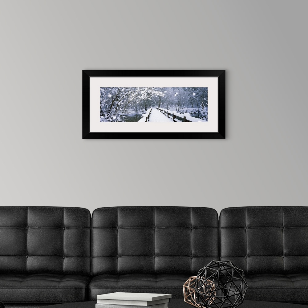 A modern room featuring Panoramic photograph of a wintry landscape of trees surrounding a snow covered footbridge as it c...
