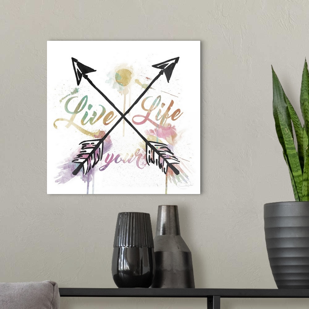 A modern room featuring "Live Your Life" watercolor painting with black crisscross arrows splitting up the words.
