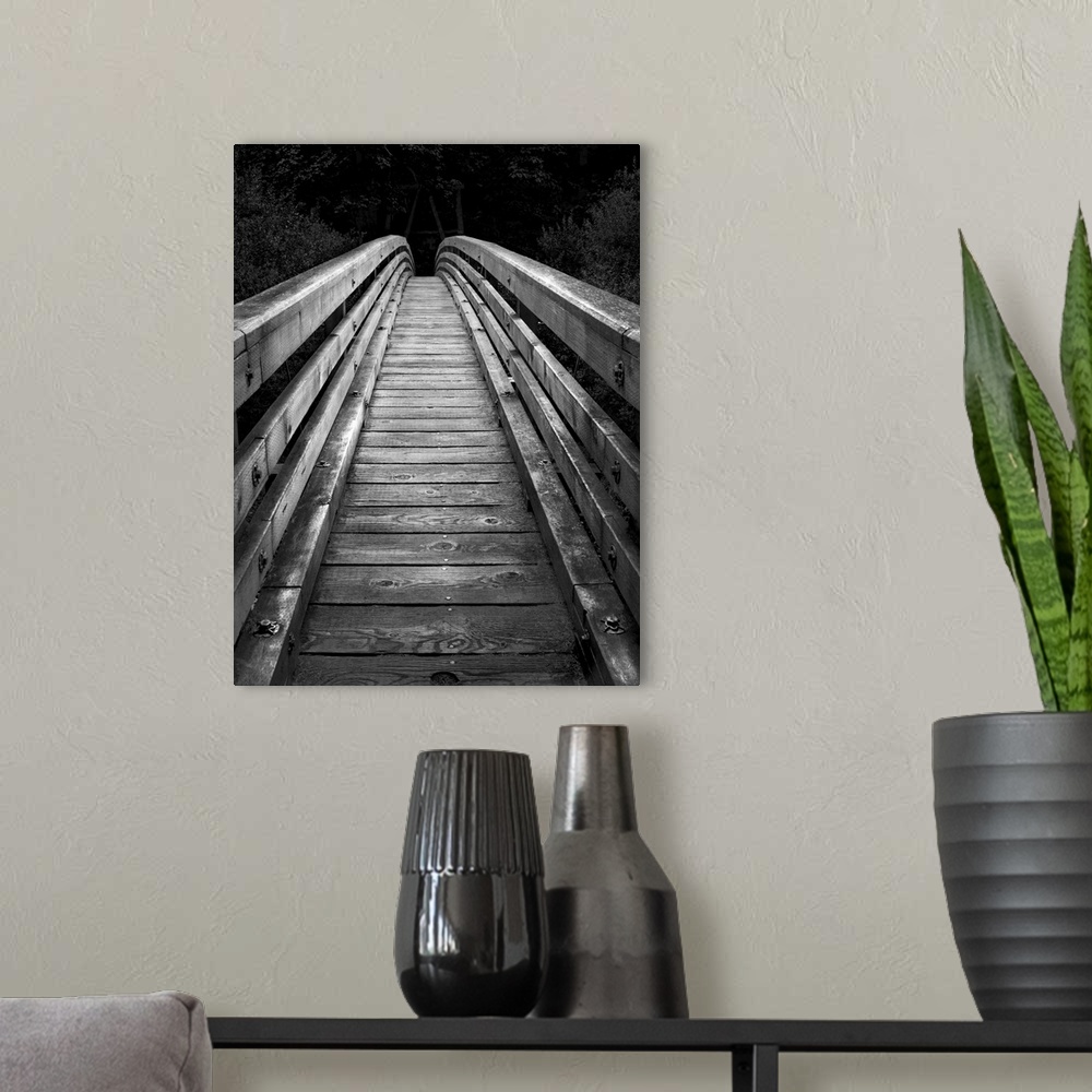 A modern room featuring An artistic black and white photograph of of a wooden bridge with a narrow walk leading into dark...