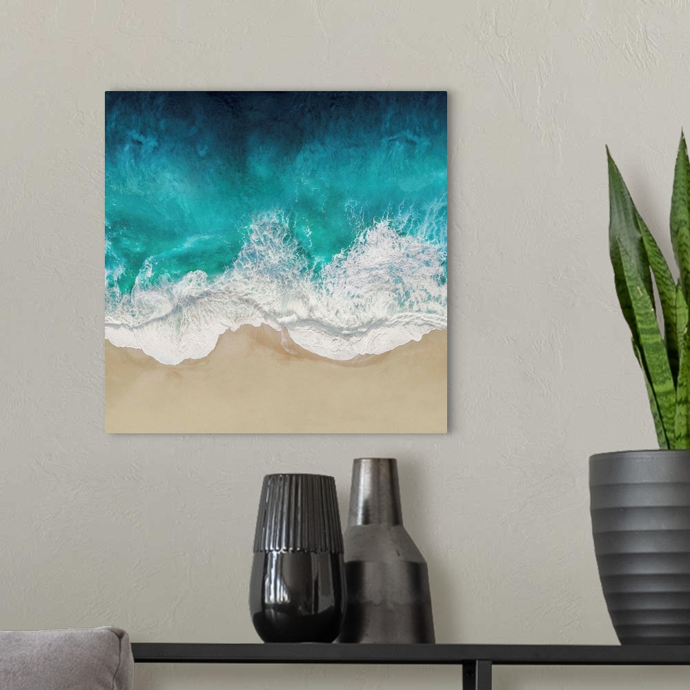 A modern room featuring One artwork in a series of aerial shots of a beach as vibrant blue waves break upon the shore.