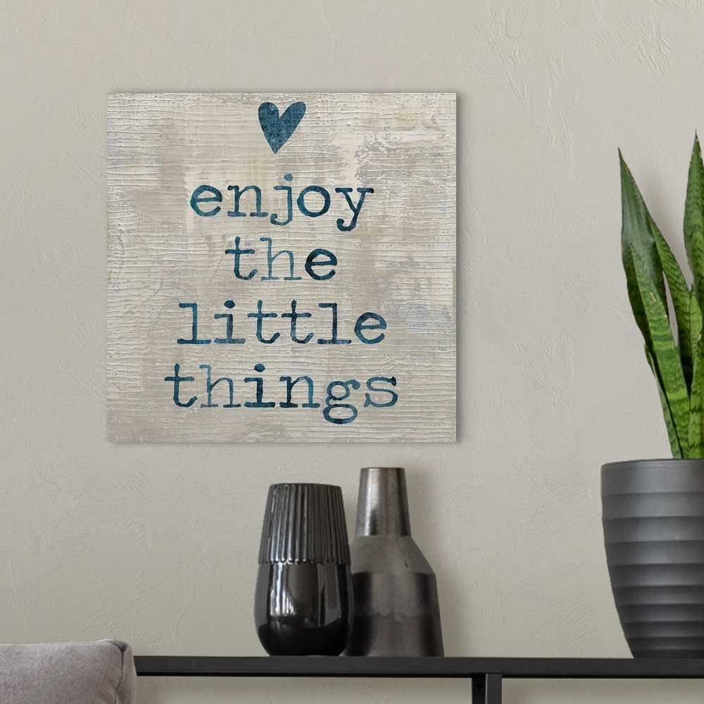 A modern room featuring "enjoy the little things" written in blue with a heart above, on a textured neutral colored backg...