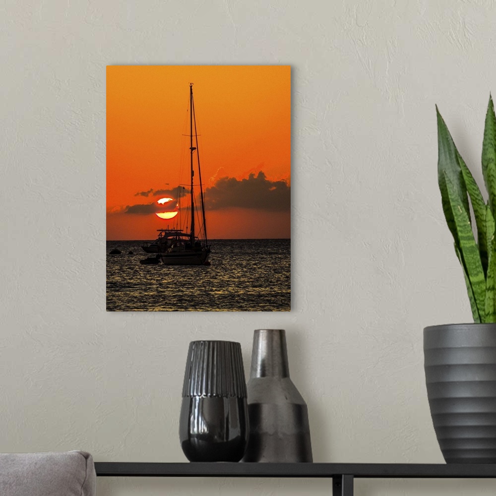 A modern room featuring Seven Mile Beach, Grand Cayman. Sailboat and a boat with the orange sun setting behind the clouds...