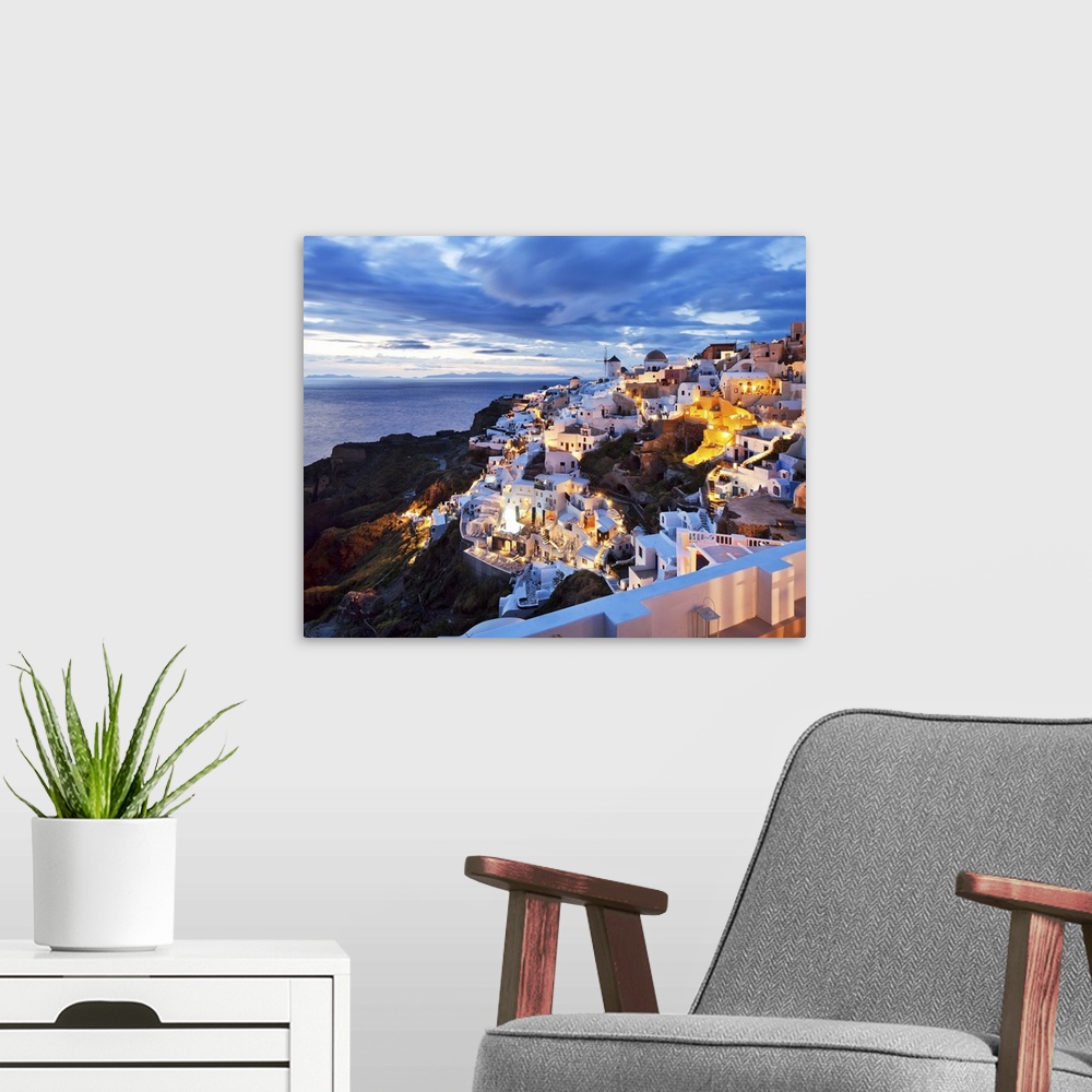 A modern room featuring Greece, Aegean islands, Cyclades, Santorini island, Greek Islands, Oia village illuminated at dusk.