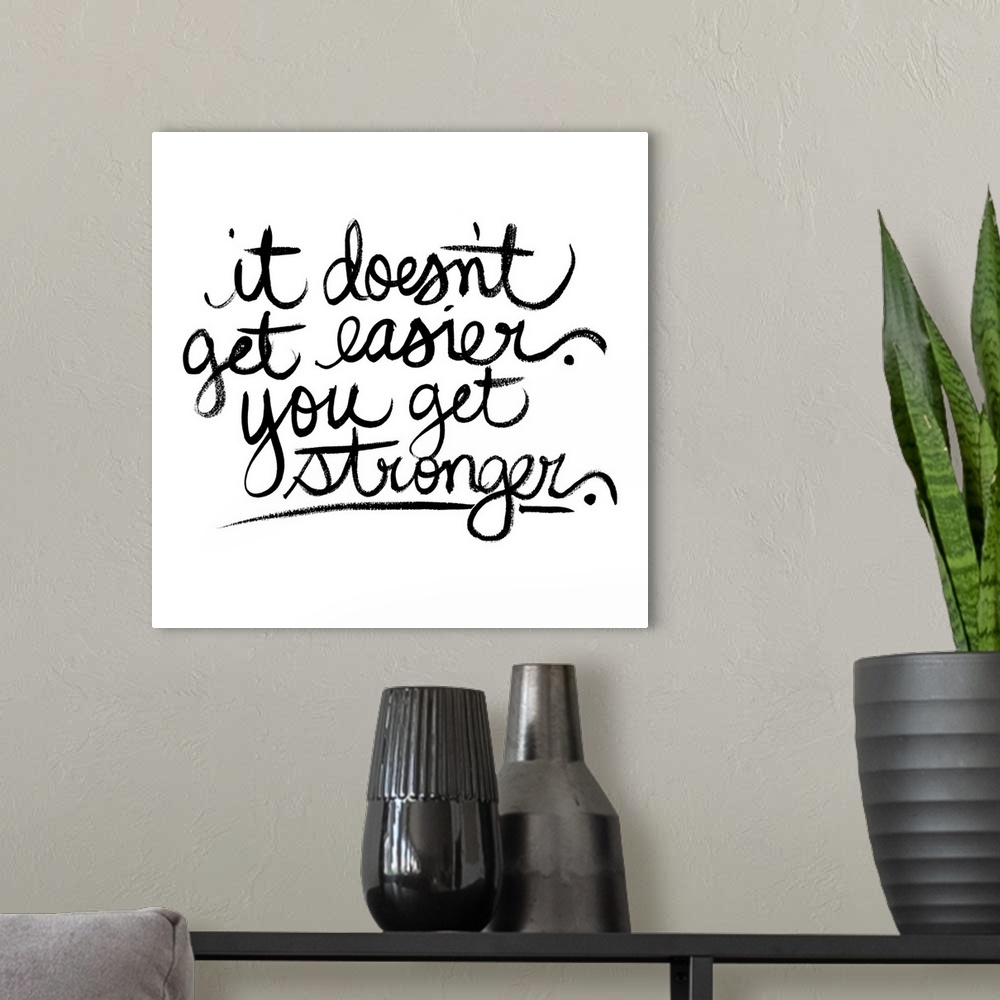 A modern room featuring Square decor with black handwritten text reading "it doesn't get easier. you get stronger" on a s...