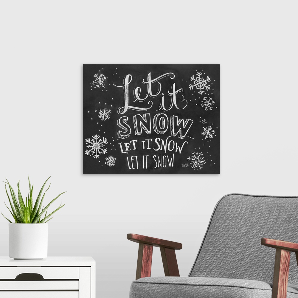 A modern room featuring "Let it snow" handwritten with several snowflakes in white chalk on a black background.