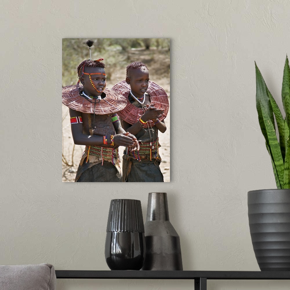 A modern room featuring Two young Pokot girls wearing traditional ornaments that denote their unmarried status. Their bro...