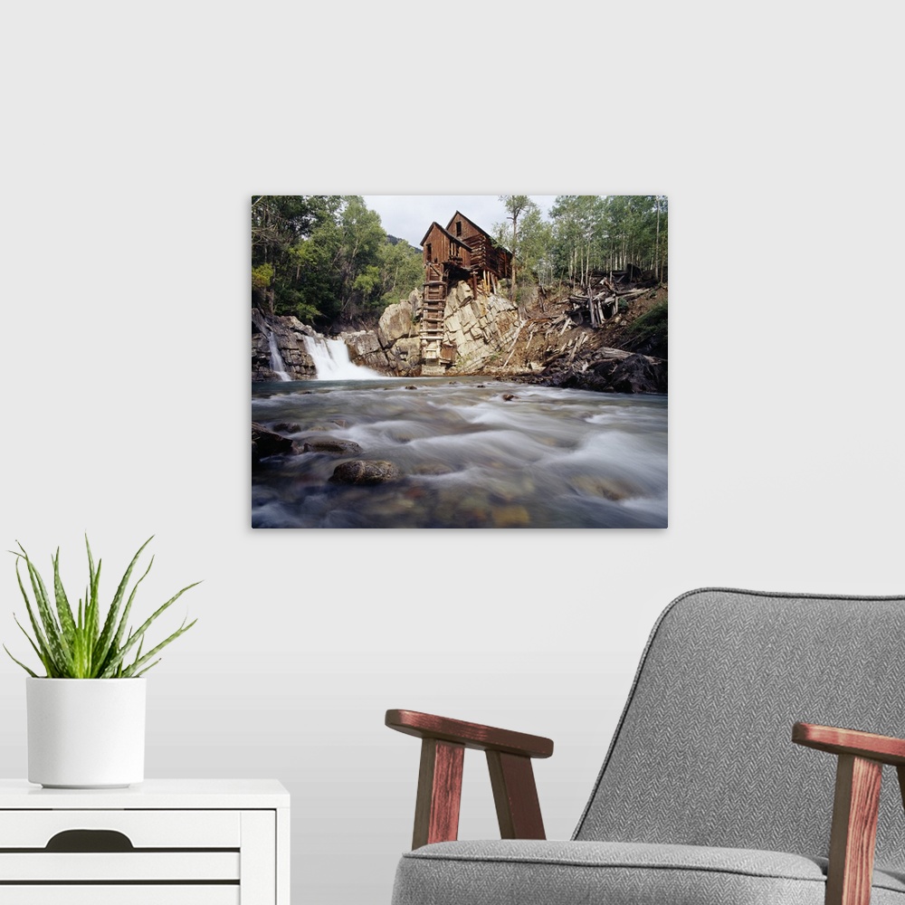 A modern room featuring Photograph of old log cabin sitting on top of rocky hill with rushing stream below.