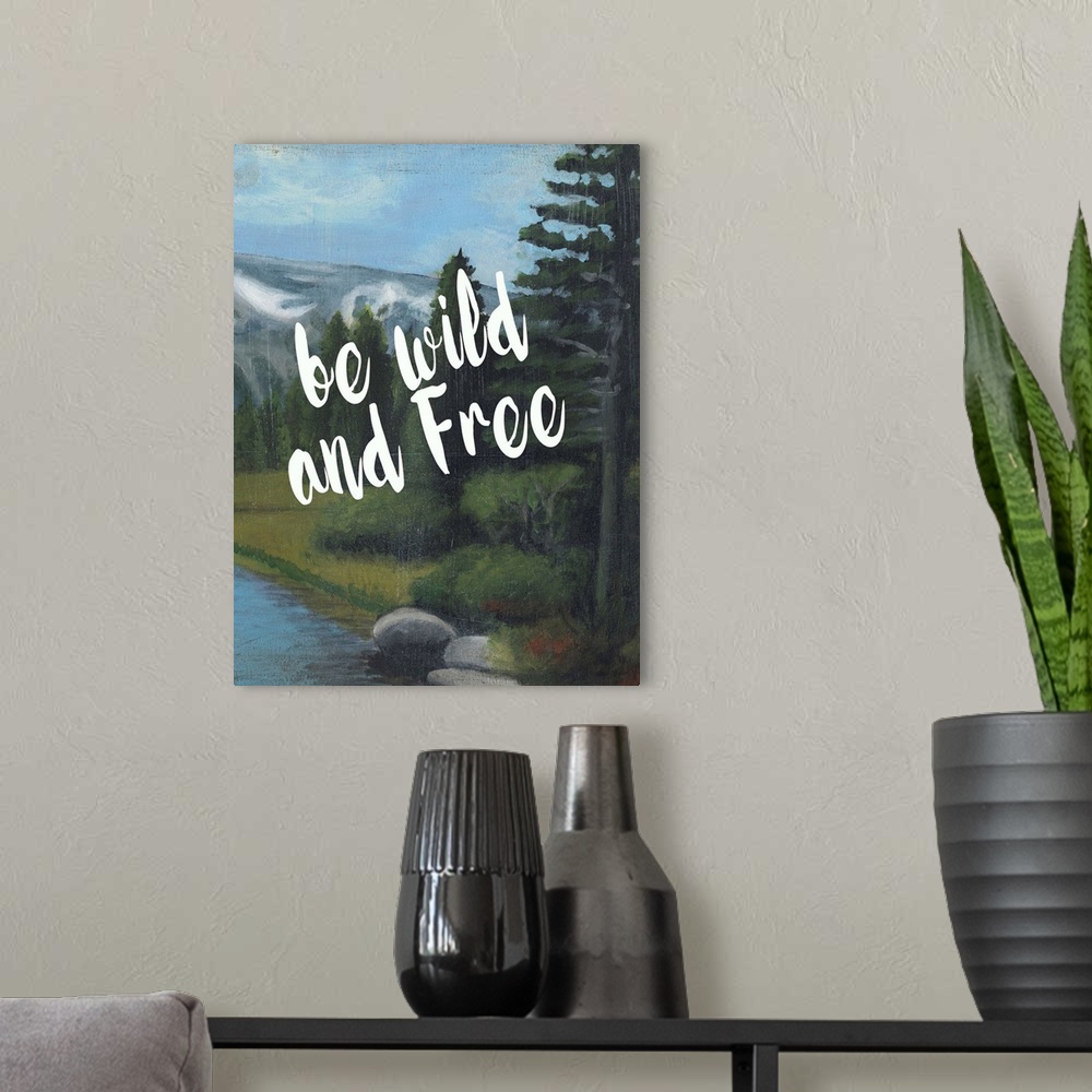 A modern room featuring White handlettered text reading "Be wild and free" over a painting of a mountain landscape.