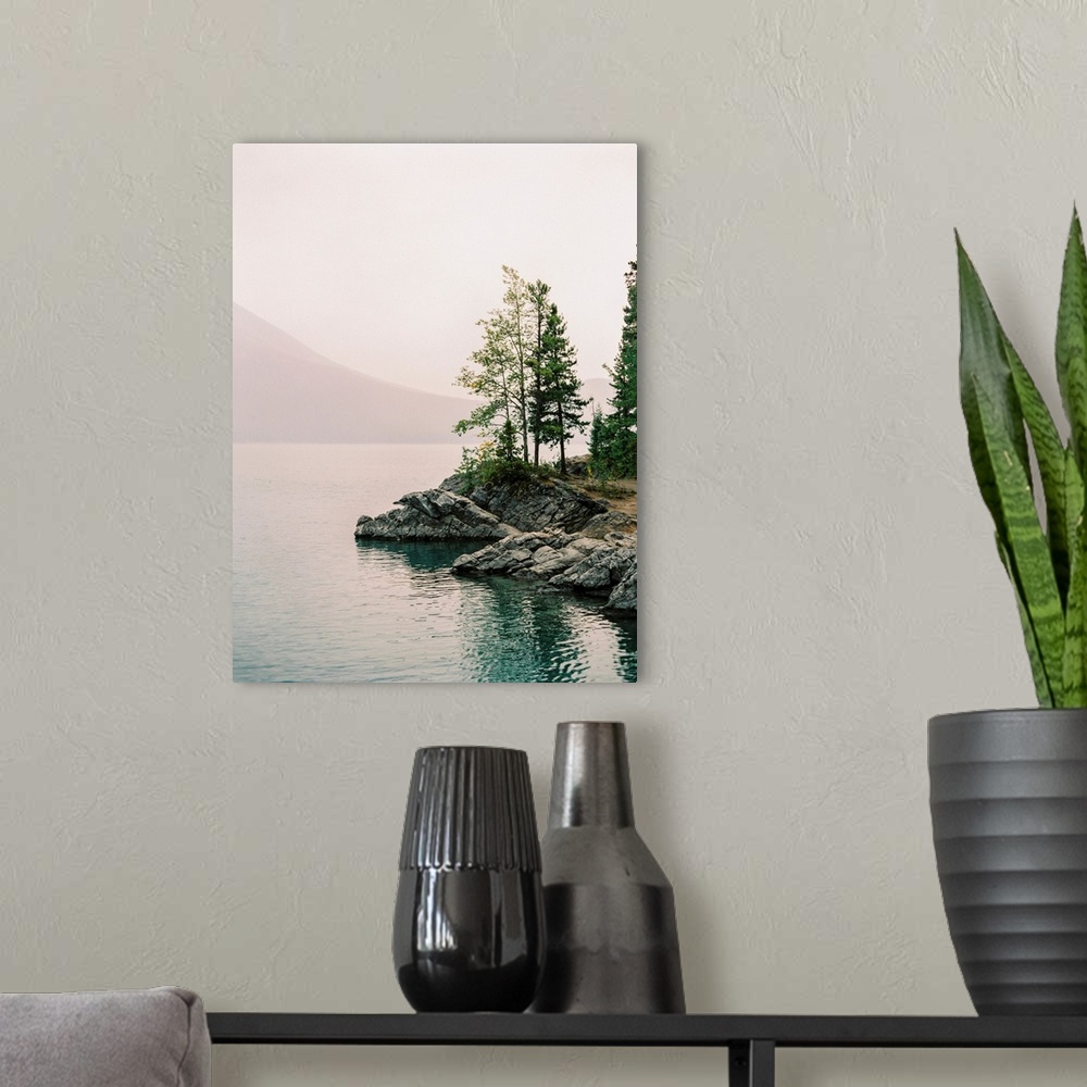 A modern room featuring A serene photograph of small trees on the rocky edge of a calm lake with a hazy sky.
