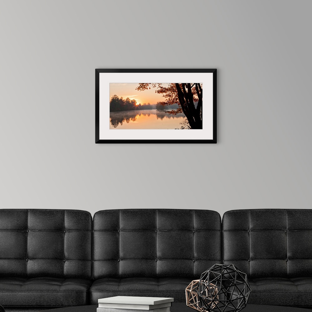 A modern room featuring Big Canvas photo of a tranquil lake at sunrise with forests around it bathed in warm sunlight.