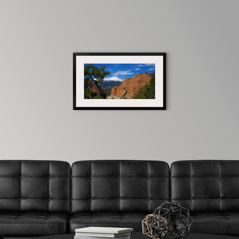 A modern room featuring Landscape wall art of trees growing among rocks in wilderness with snowcapped peaks in the backgr...