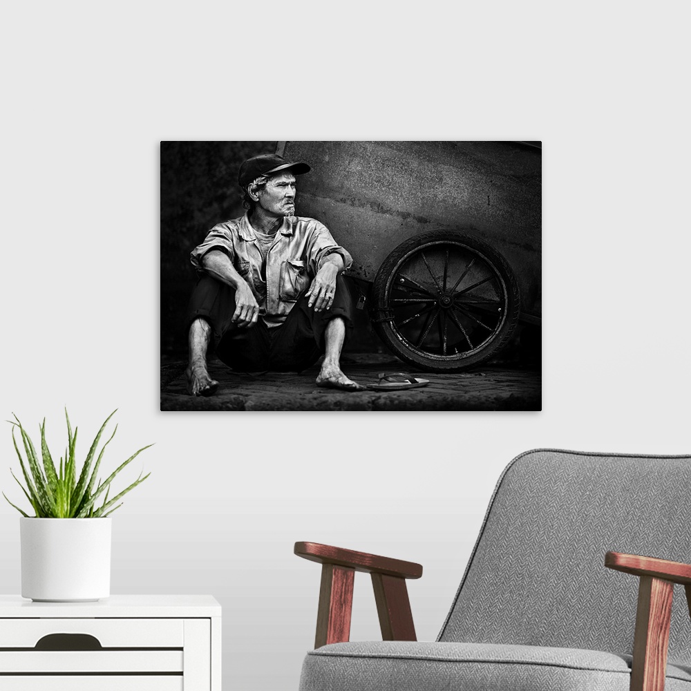 A modern room featuring A barefoot man sitting in the street next to the wheel of his wagon in Jakarta, Indonesia.