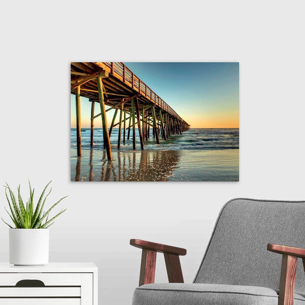 A modern room featuring A photograph of a long pier jetting out over the ocean. Sunlight glowing over the horizon as the ...