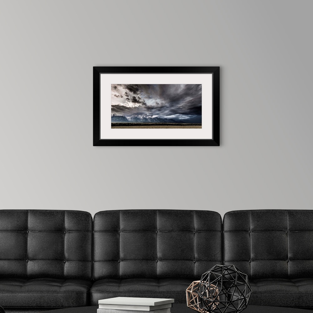 A modern room featuring Landscape photograph of a field in front of snow capped mountains with a dramatic stormy sky above.