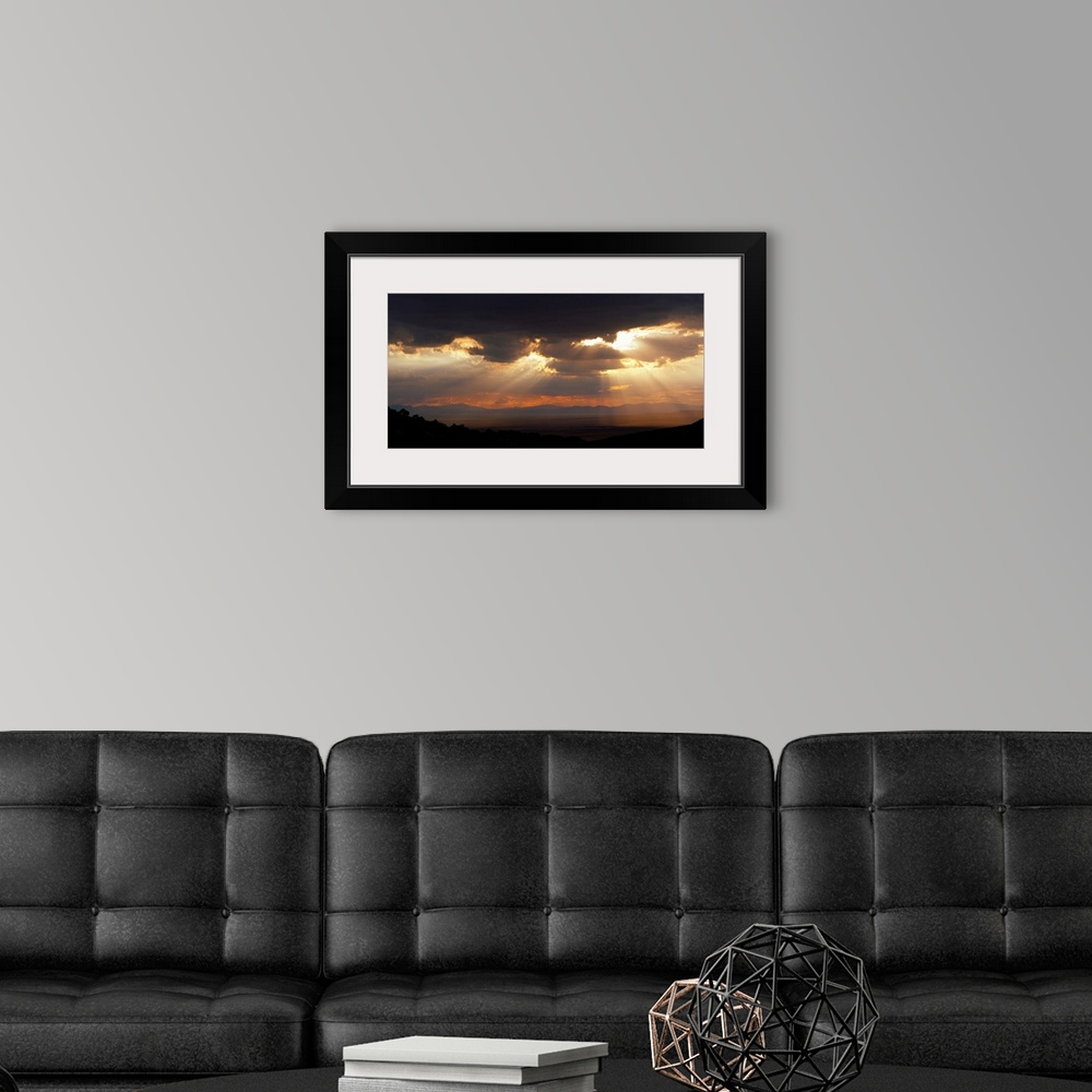 A modern room featuring Horizontal, large photograph of sunlight beaming through a sky full of huge, dark clouds, over th...