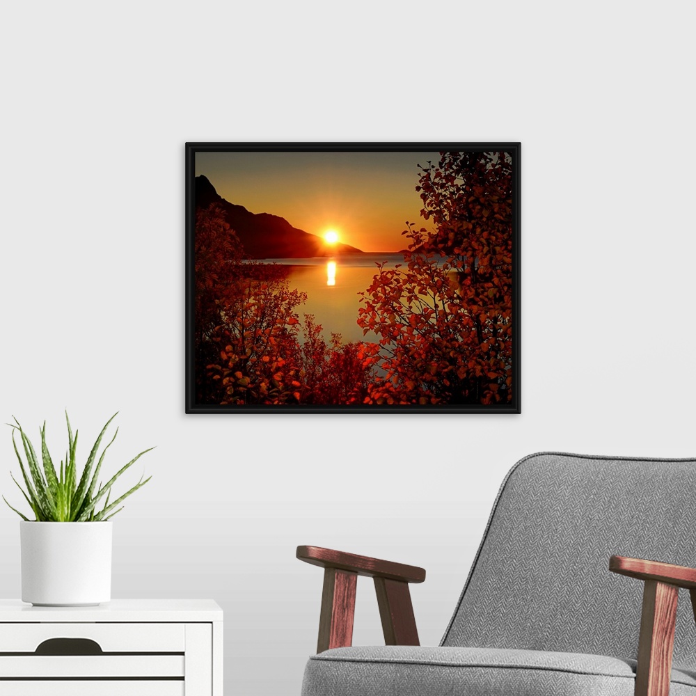 A modern room featuring Big photograph emphasizes the sun as it begins to set over a mountain and then reflect over a cal...