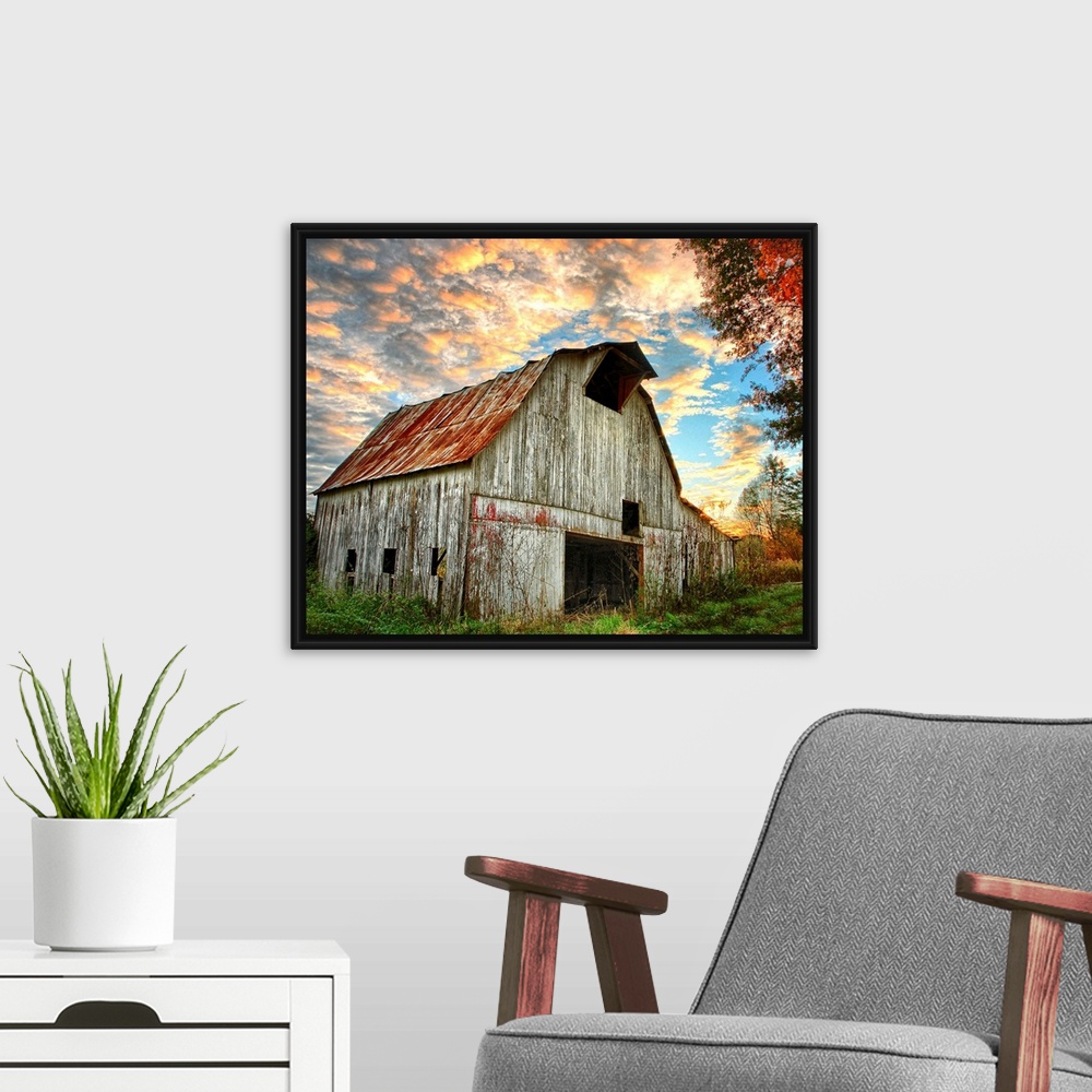 A modern room featuring Sunset over an old, weathered barn, with a cloudy sky.