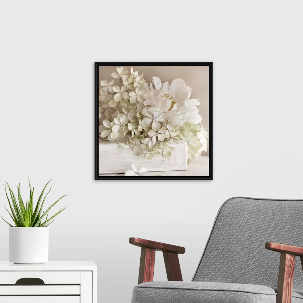 A modern room featuring Square photo on canvas of white flowers laying on top of a white book with the spine facing the c...