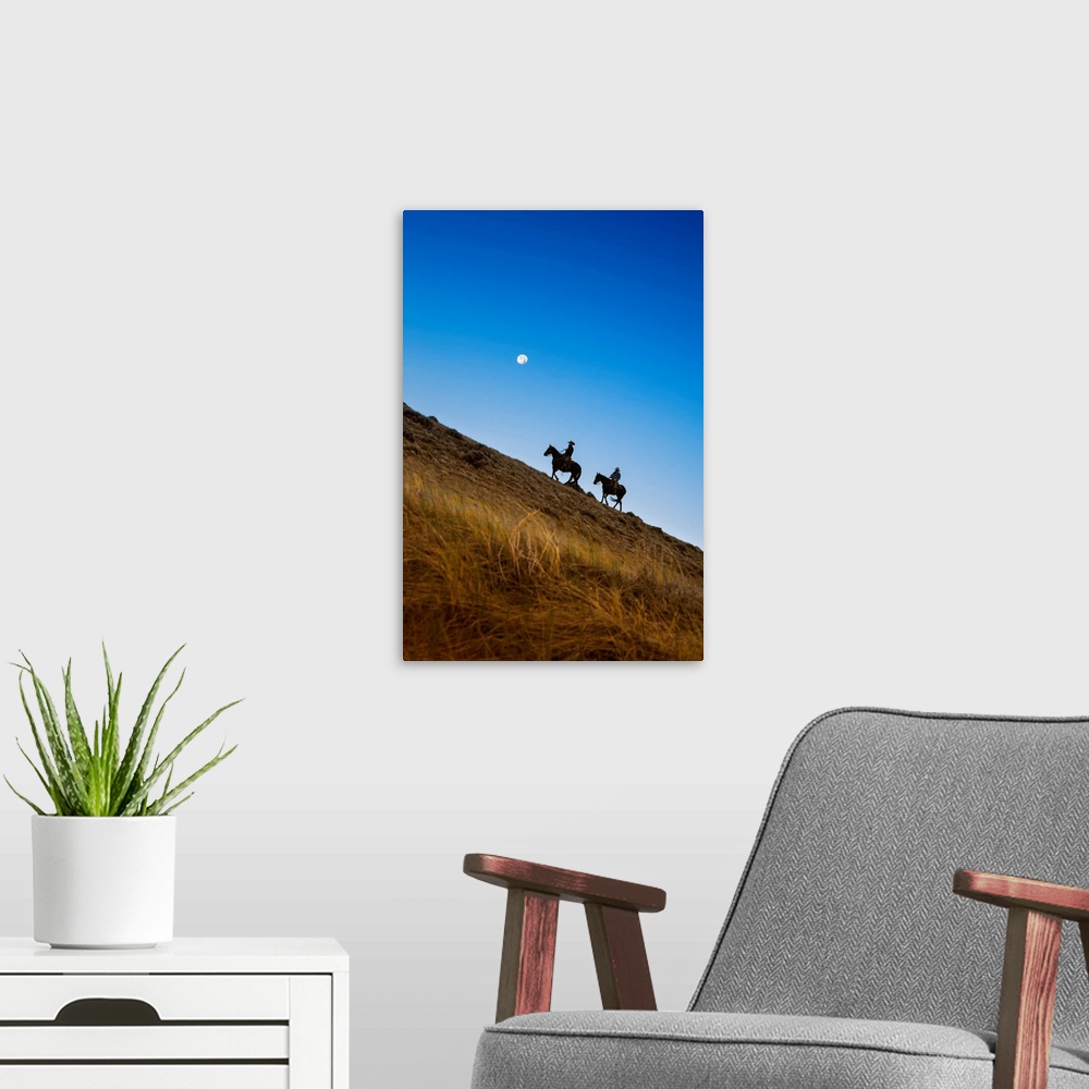 A modern room featuring Two wranglers riding horses up a hill with full moon in backround at blue hour