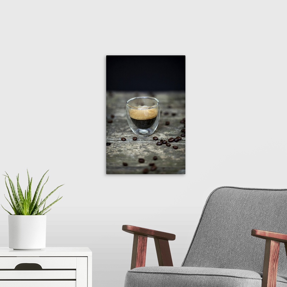A modern room featuring Close-up of typical espresso coffee in glass cup amongst raw coffee beans on wooden table and bla...