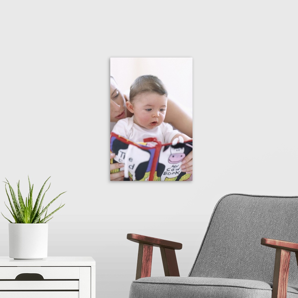 A modern room featuring Mother reading to baby boy. Faces of a mother reading aloud to her 6-month-old baby boy. Describi...