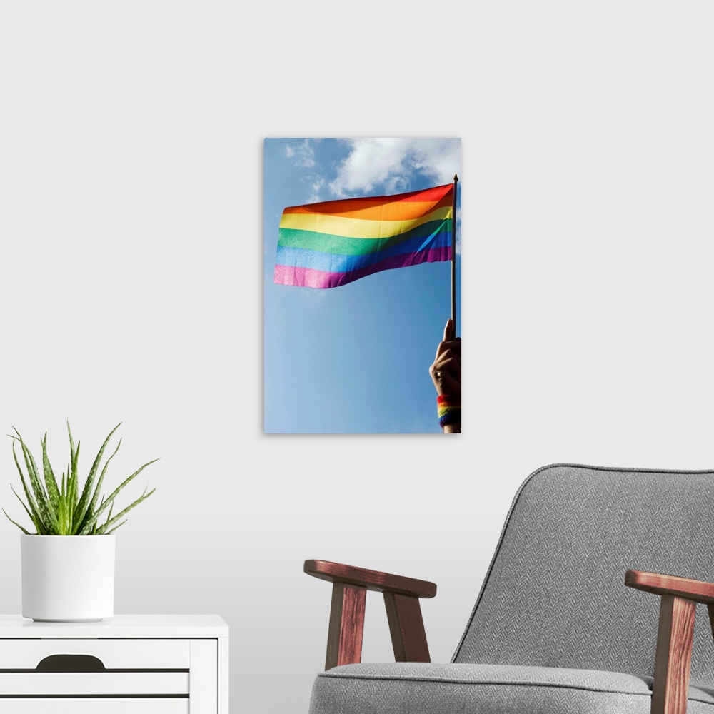 A modern room featuring Person's hand holding rainbow-colored flag waving in the sky