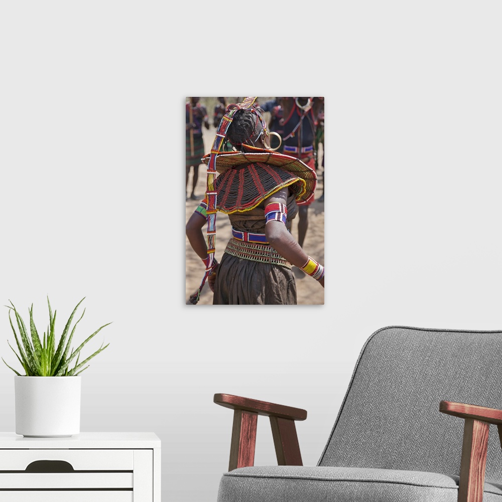 A modern room featuring A Pokot woman in traditional attire dances to celebrate an Atelo ceremony. Her broad belt is made...
