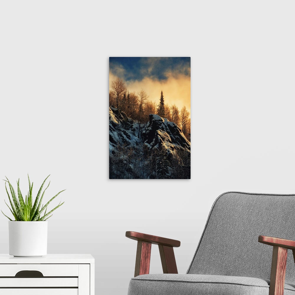 A modern room featuring Clouds lit up with fading sunlight over a forest near snowy rocks on a mountainside.