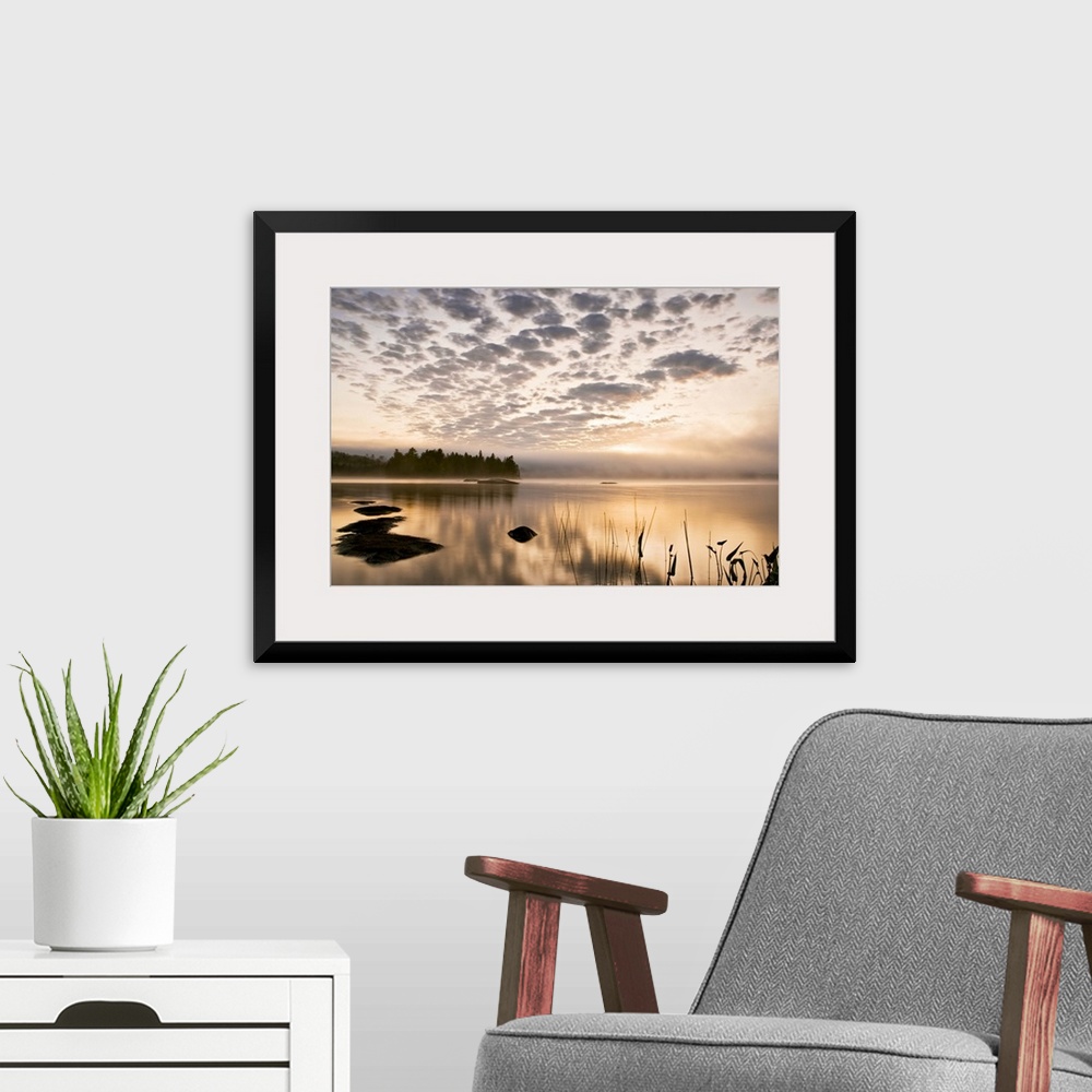 A modern room featuring Horizontal photograph on a big wall hanging of the sun set reflecting in a large body of water, a...