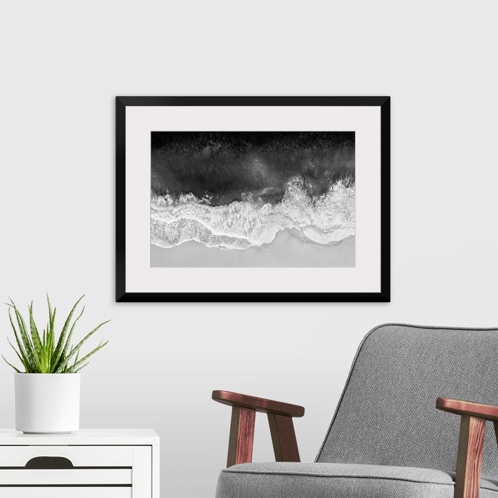 A modern room featuring One artwork in a series of aerial shots of a beach as dark gray waves break upon the shore.