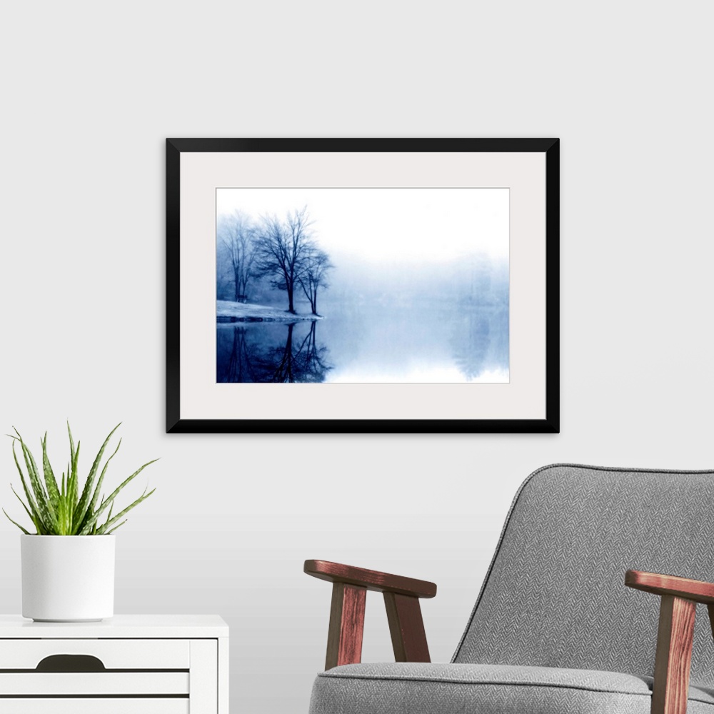 A modern room featuring A photograph taken of a lake with bare trees off to the left side and more trees behind dense fog...