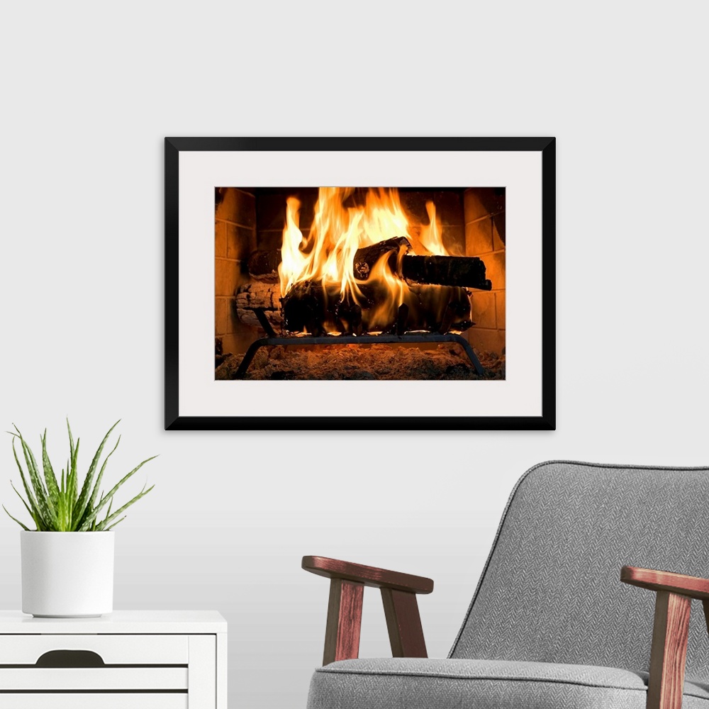 A modern room featuring A horizontal photograph of logs burning inside a personal, home fireplace lined with bricks