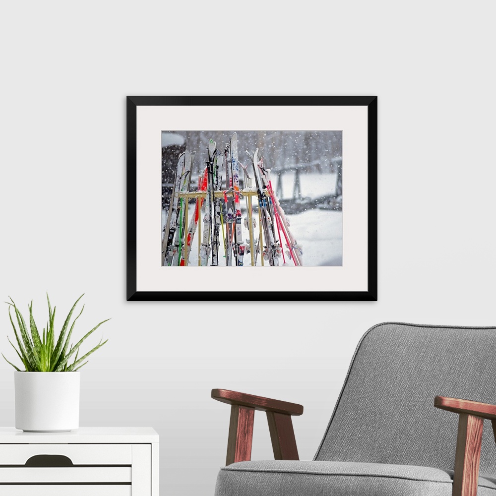 A modern room featuring In this photograph multiple skis are stored on an outside rack as large white snowflakes fall all...