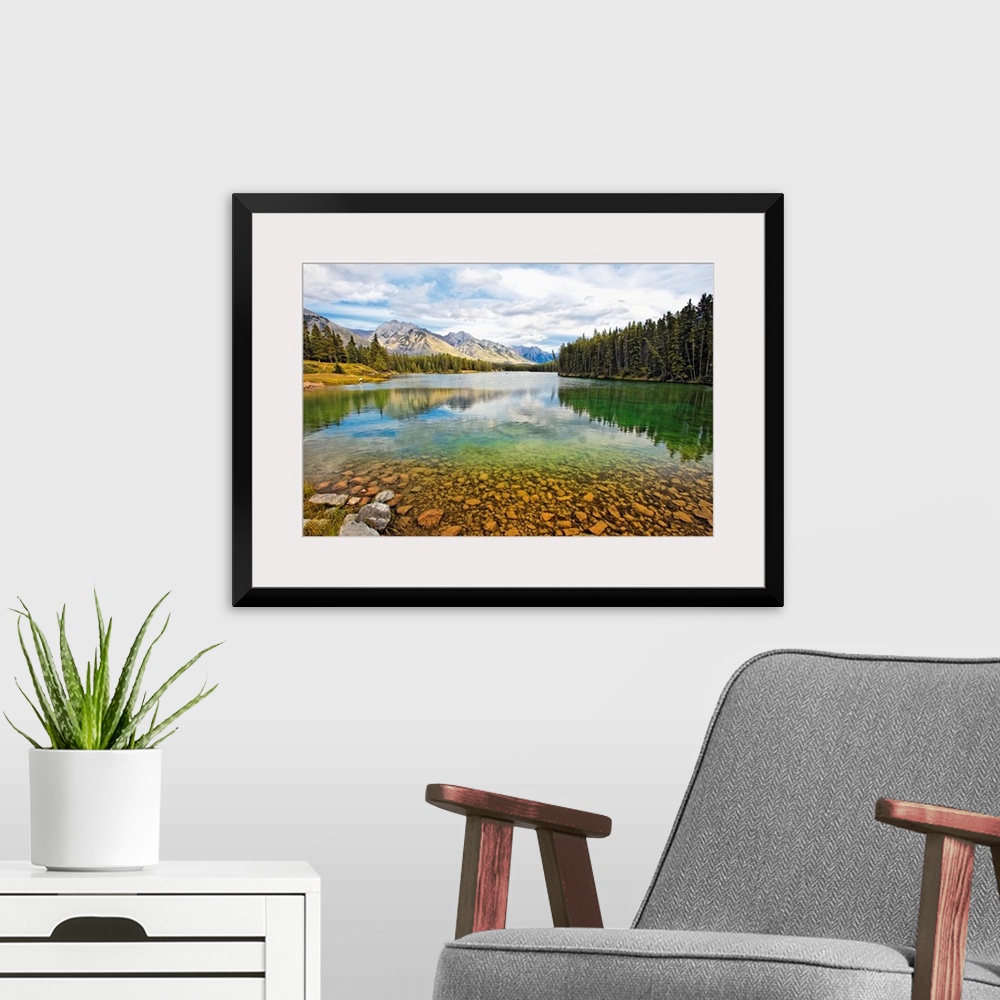 A modern room featuring Giant photograph taken from the rocky shores of a lake that is surrounded by dense forests and sn...