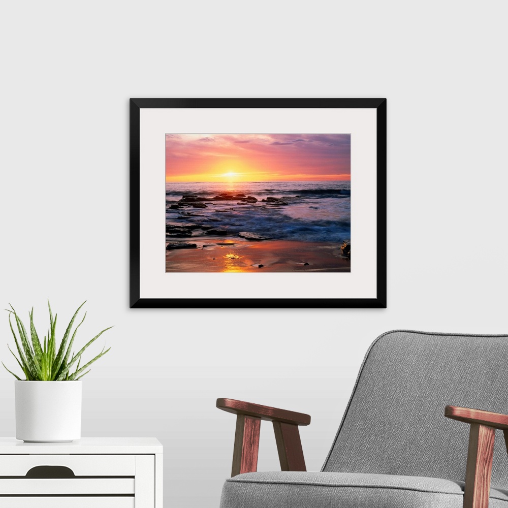 A modern room featuring Photograph of rocky shoreline at sunset with a cloudy sky.