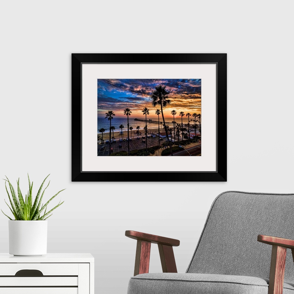 A modern room featuring A single image aerial sunset capture of tall palms silhouetted against colorful clouds near Ocean...