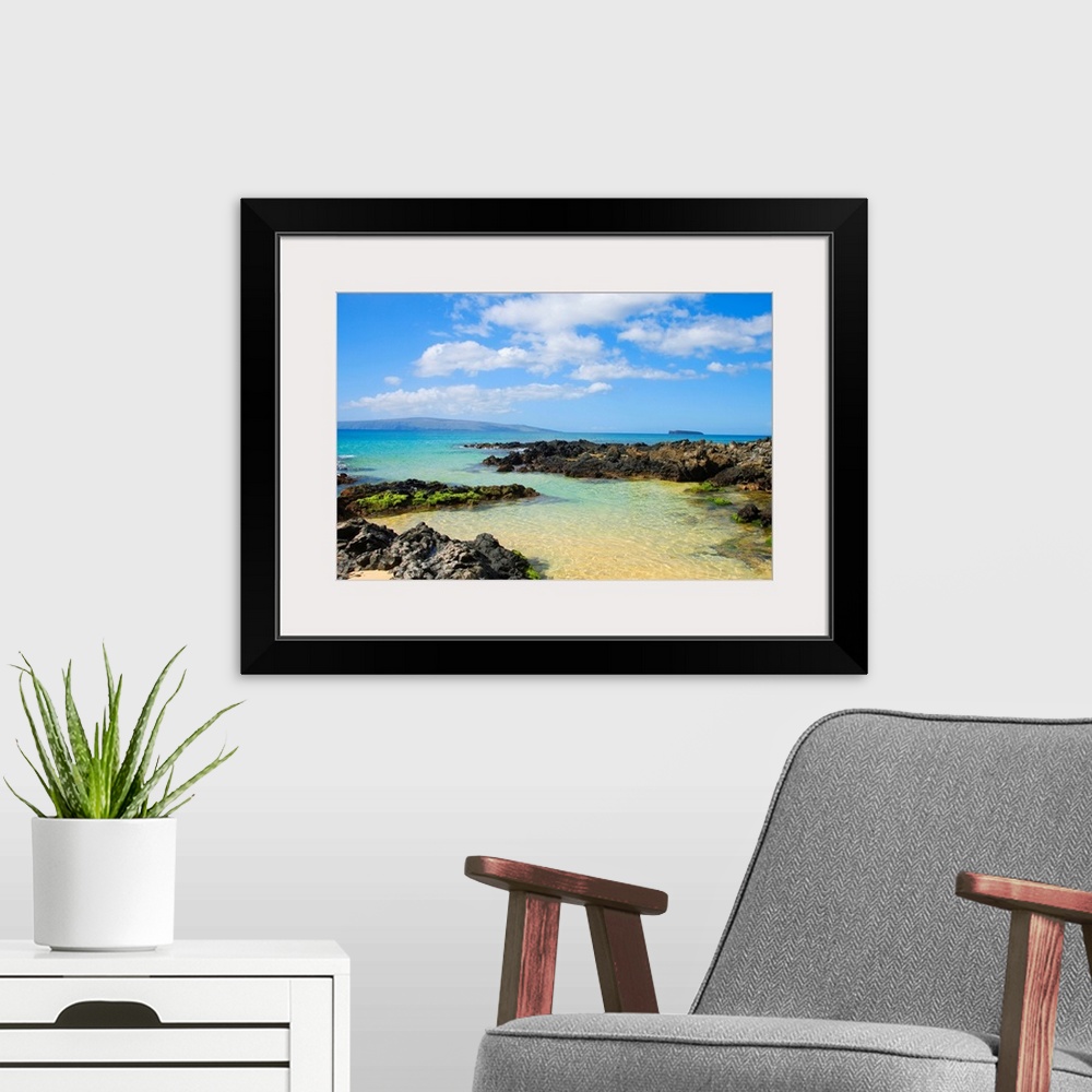 A modern room featuring Photograph of rocky shoreline with crystal clear water and mountains in the distance under a clou...
