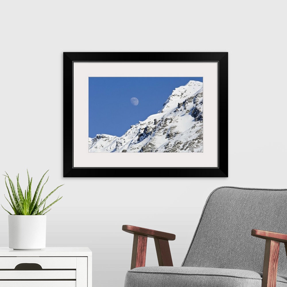 A modern room featuring Moon rising over snow covered mountain peak at Hatcher Pass in Southcentral Alaska.
